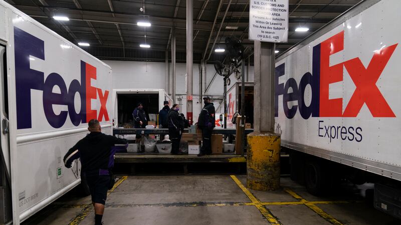 FILE - FedEx delivery trucks are parked next to a conveyor belt while being loaded with...